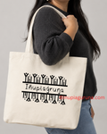 A person wearing a dark gray sweater and blue jeans carries a large off-white canvas tote bag with black printed text and decorative symbols. The bag has the text 'Iāniagāruna' printed in black.